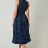 Woman wearing a navy blue dress with white polka dots on a plain background