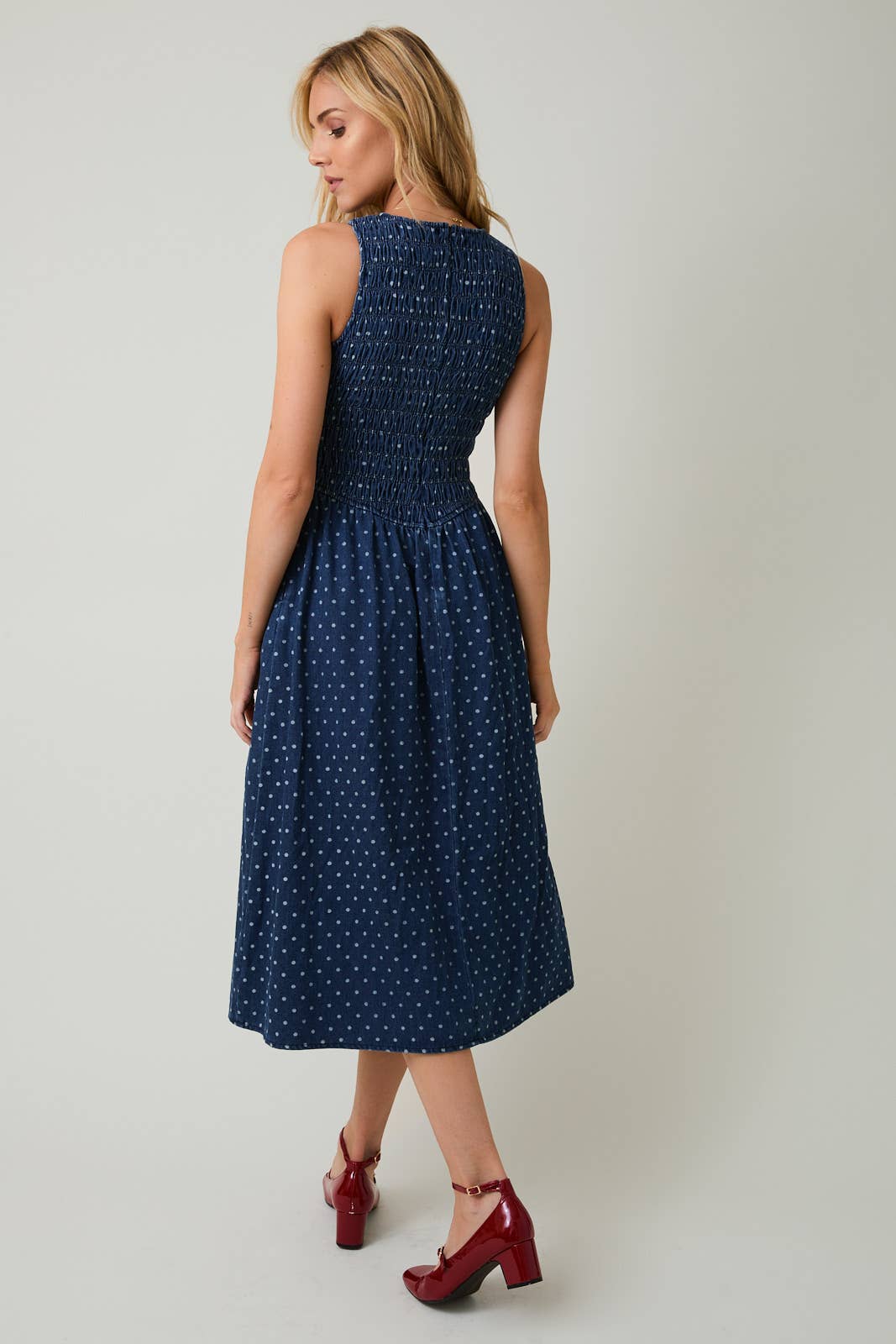 Woman wearing a navy blue dress with white polka dots on a plain background