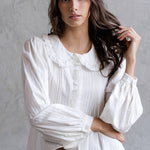 Woman wearing a white blouse with puffed sleeves against a gray background