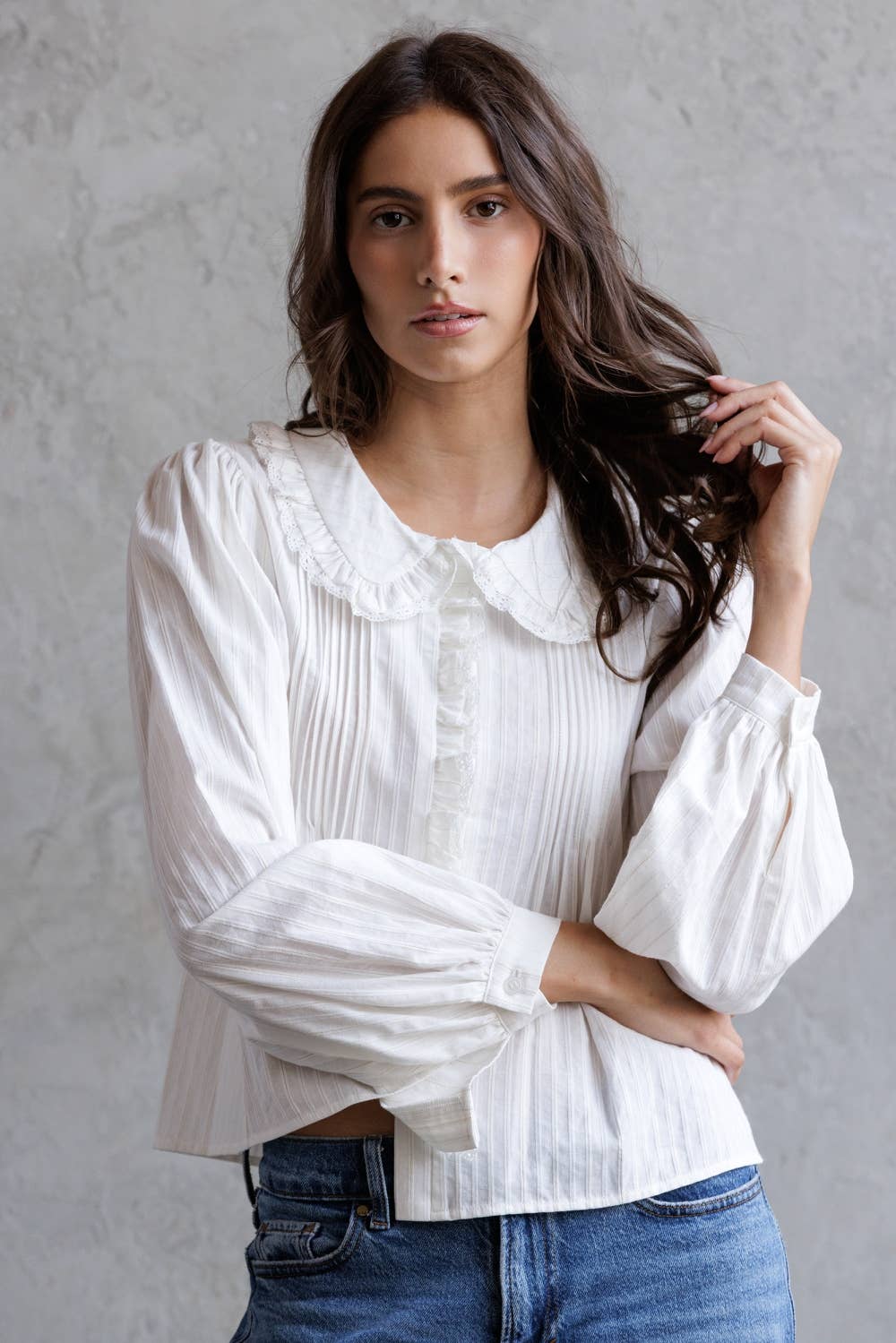 Woman wearing a white blouse with puffed sleeves against a gray background