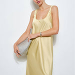 Woman wearing a light yellow satin slip dress against a white background