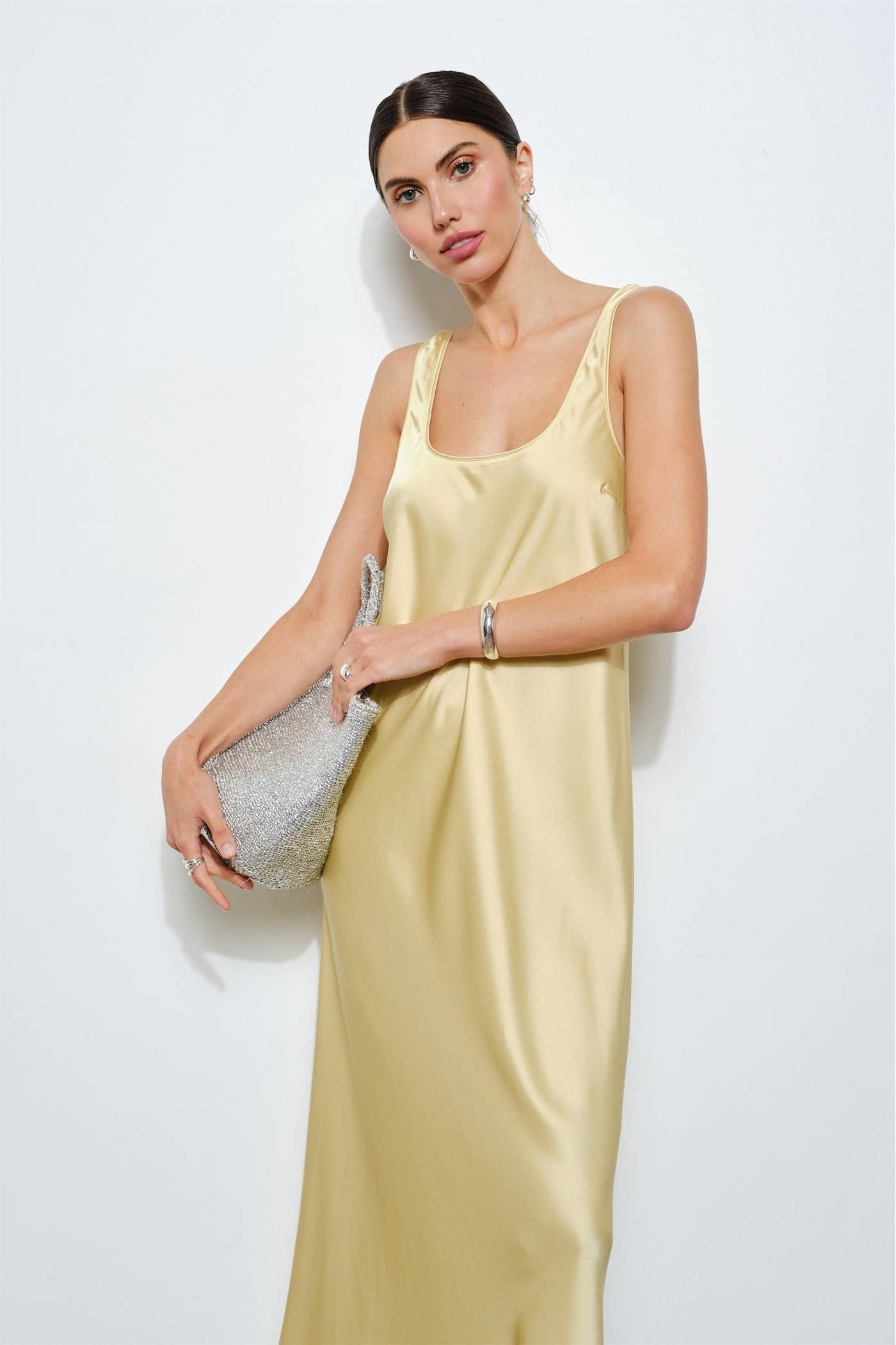 Woman wearing a light yellow satin slip dress against a white background