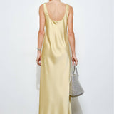 Woman wearing a light yellow dress holding a gray handbag against a white background