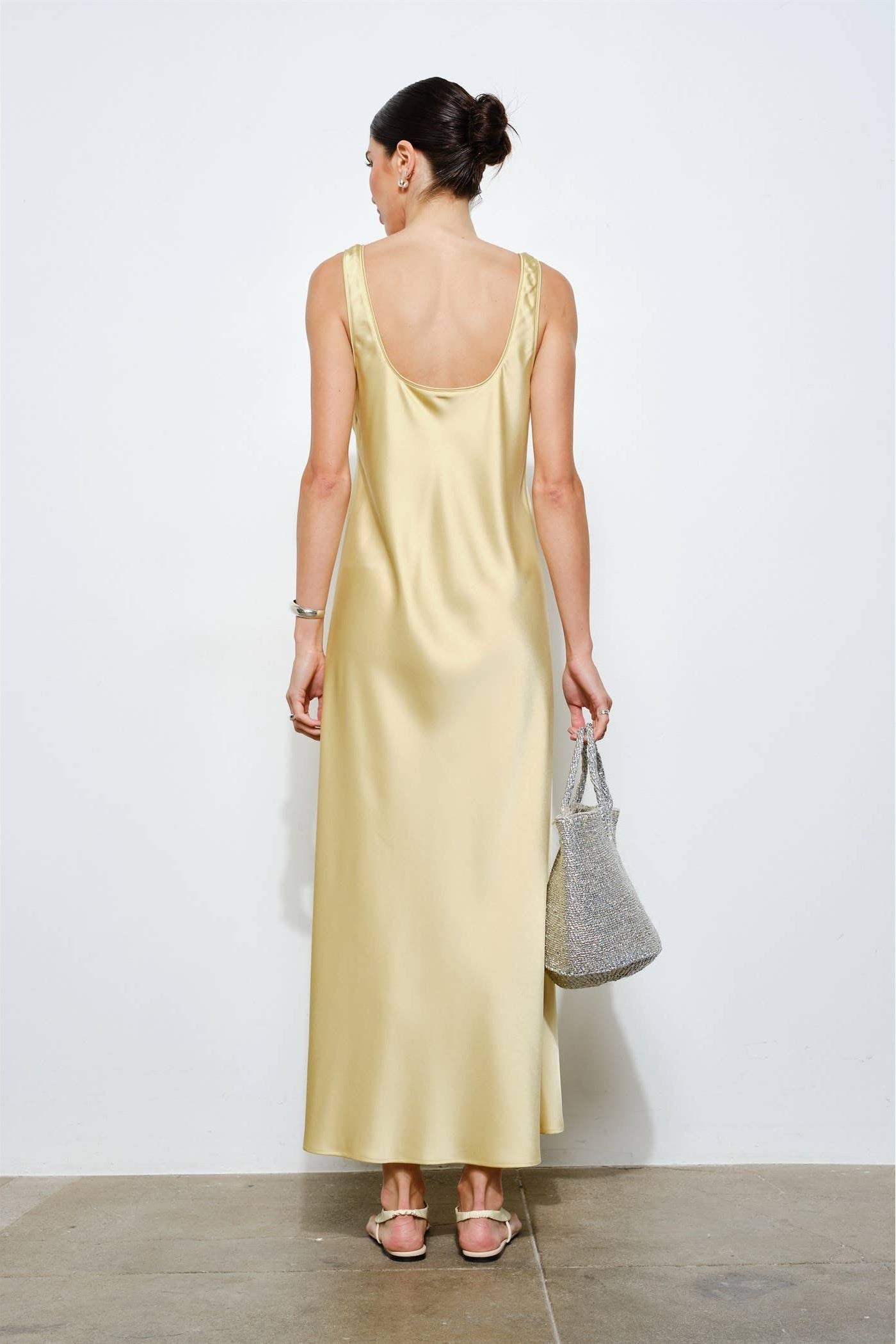 Woman wearing a light yellow dress holding a gray handbag against a white background