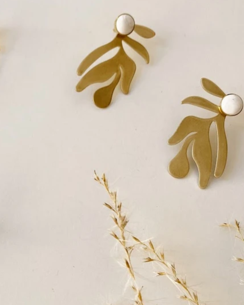 Gold and silver earrings on a light background with dried plants.