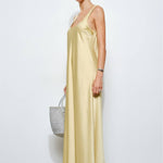 Woman wearing a long yellow dress holding a gray bag against a white background