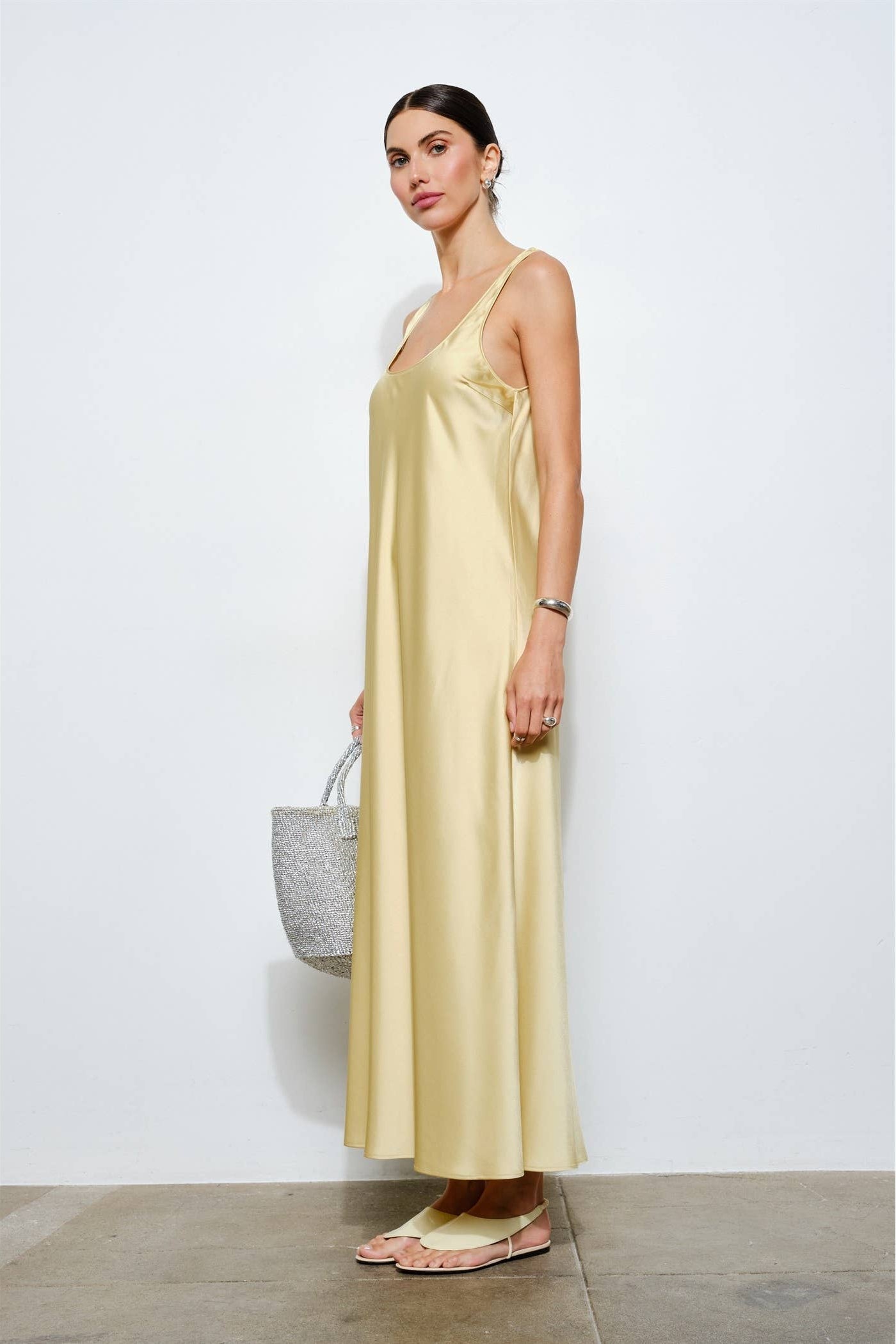 Woman wearing a long yellow dress holding a gray bag against a white background